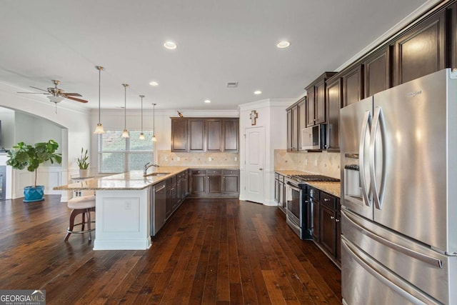 kitchen featuring ceiling fan, appliances with stainless steel finishes, a peninsula, dark brown cabinets, and light stone countertops