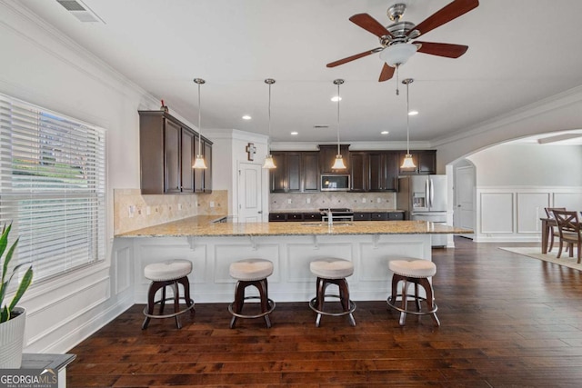 kitchen with dark brown cabinetry, a peninsula, stainless steel appliances, arched walkways, and a sink