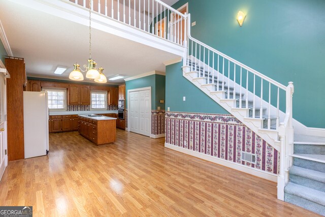 115 Flagstop Run, Fayetteville, GA 30215 - kitchen featuring appliances with stainless steel finishes, crown molding, brown cabinetry, a center island, and light wood-style flooring