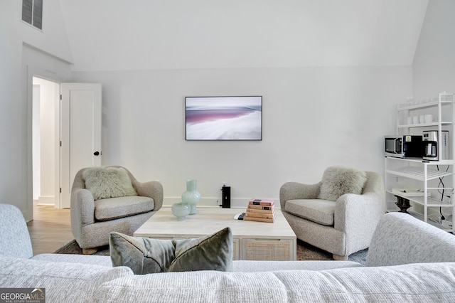 living area with baseboards, visible vents, vaulted ceiling, and wood finished floors