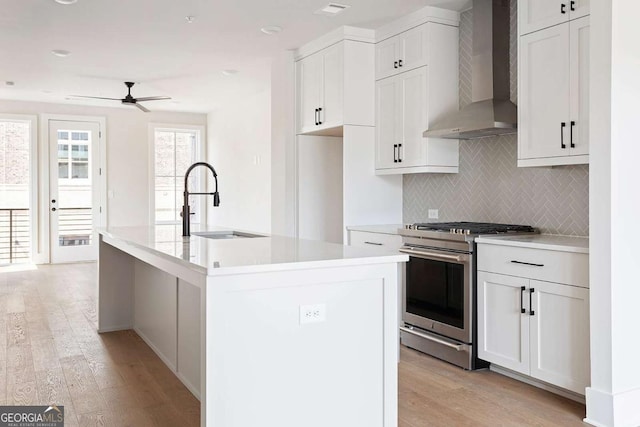 kitchen featuring stainless steel range with gas cooktop, wall chimney range hood, a sink, ceiling fan, and decorative backsplash
