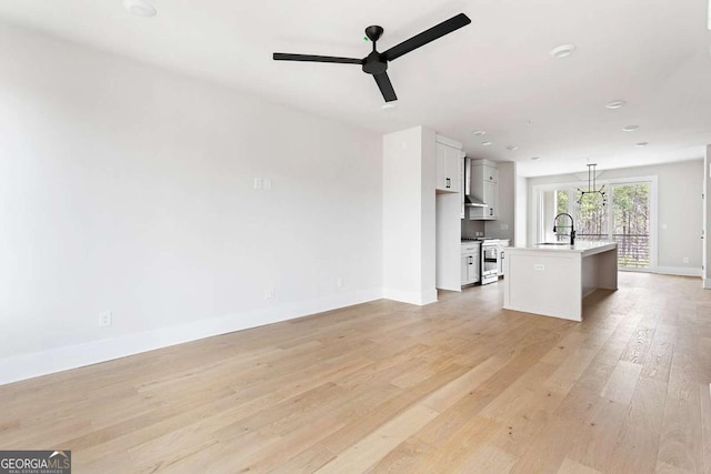 unfurnished living room featuring a sink, a ceiling fan, baseboards, and light wood-style flooring