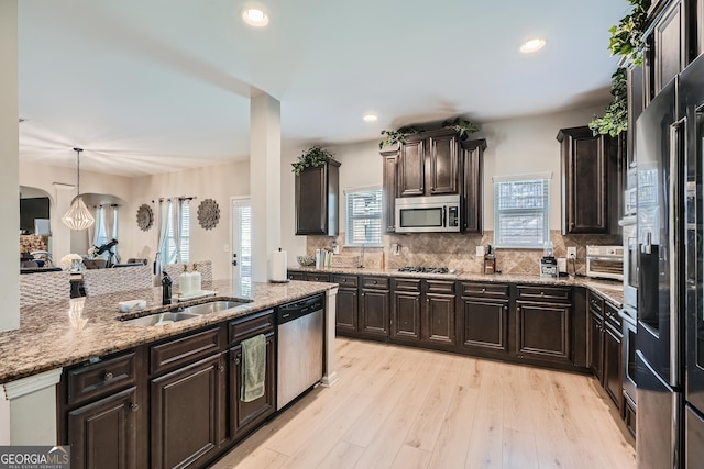 kitchen with stainless steel appliances, a sink, tasteful backsplash, dark brown cabinetry, and light stone countertops