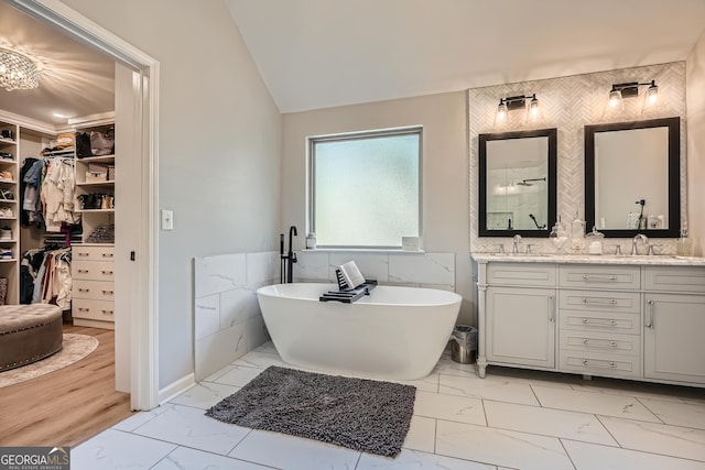 full bath featuring a spacious closet, marble finish floor, double vanity, tile walls, and a soaking tub
