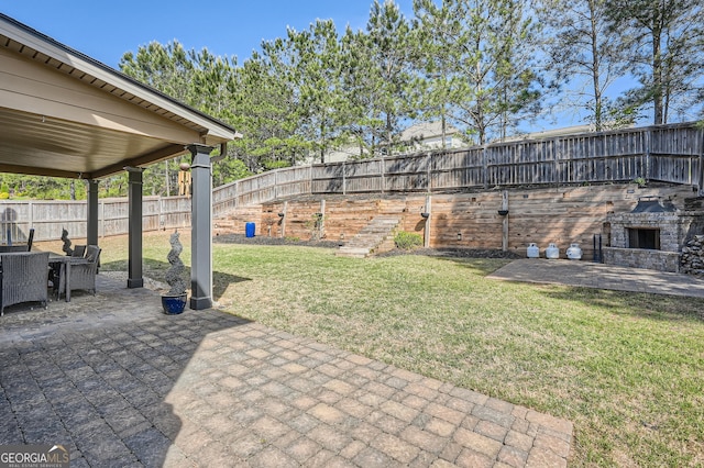 view of yard with a fenced backyard, an outdoor stone fireplace, and a patio