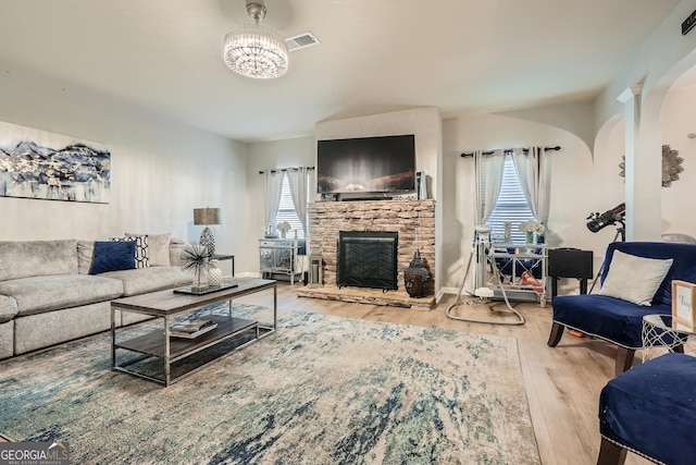 living room featuring wood finished floors, a stone fireplace, visible vents, and plenty of natural light