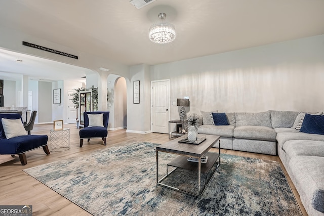 living area with arched walkways, visible vents, baseboards, a chandelier, and wood finished floors
