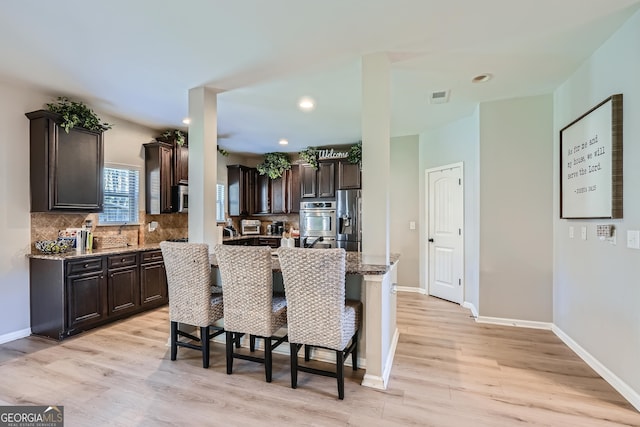 kitchen featuring light wood-type flooring, stainless steel refrigerator with ice dispenser, dark brown cabinetry, and a breakfast bar area
