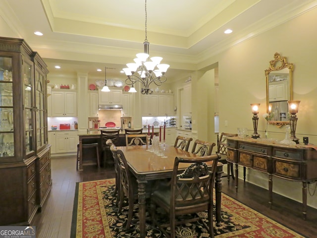 dining space with a tray ceiling, crown molding, dark wood-type flooring, and an inviting chandelier