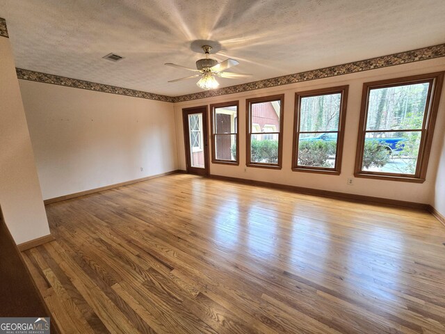 unfurnished room with wood finished floors, a textured ceiling, baseboards, visible vents, and ceiling fan