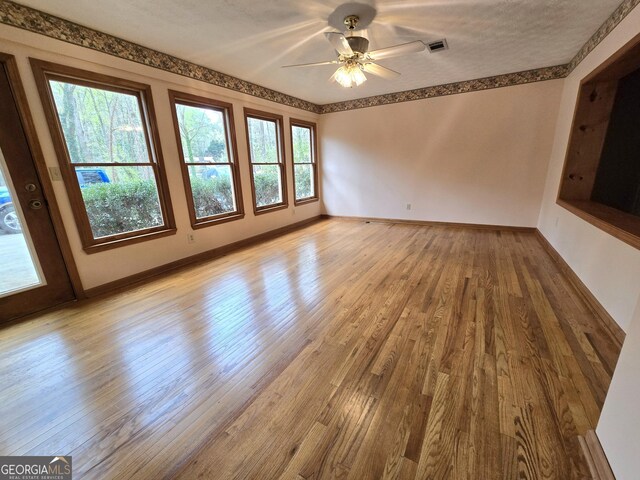 unfurnished living room featuring hardwood / wood-style floors, baseboards, ceiling fan, and a wealth of natural light