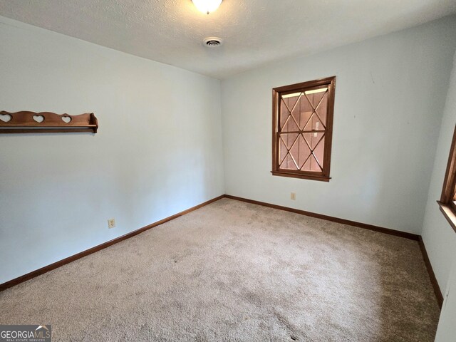 carpeted spare room featuring baseboards, a textured ceiling, and visible vents
