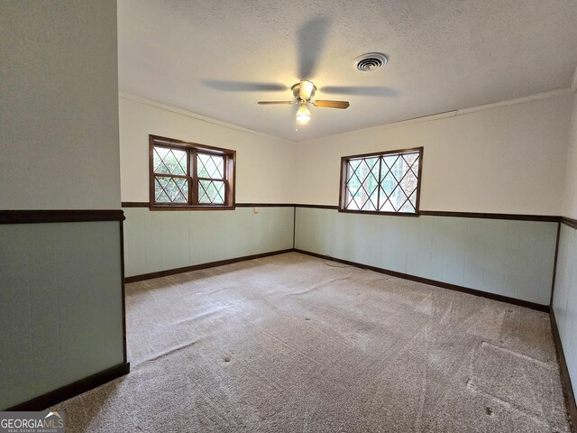 spare room featuring a textured ceiling, carpet floors, visible vents, a ceiling fan, and wainscoting