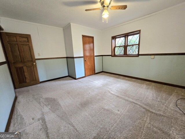 spare room with a ceiling fan, carpet floors, crown molding, and baseboards