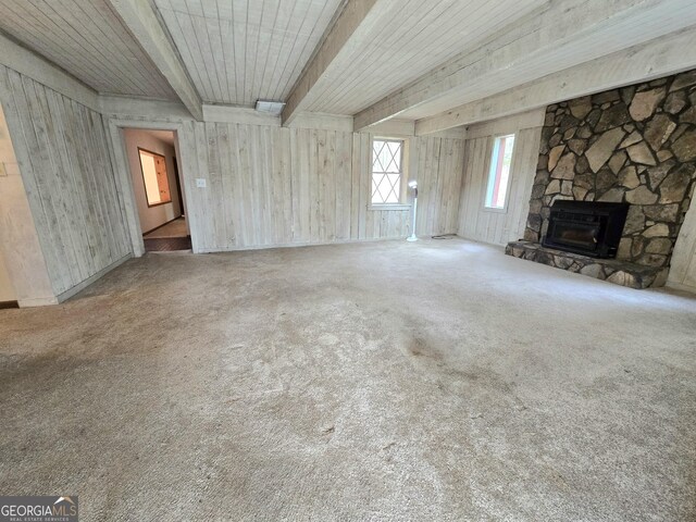 unfurnished living room featuring a stone fireplace, beamed ceiling, and carpet floors