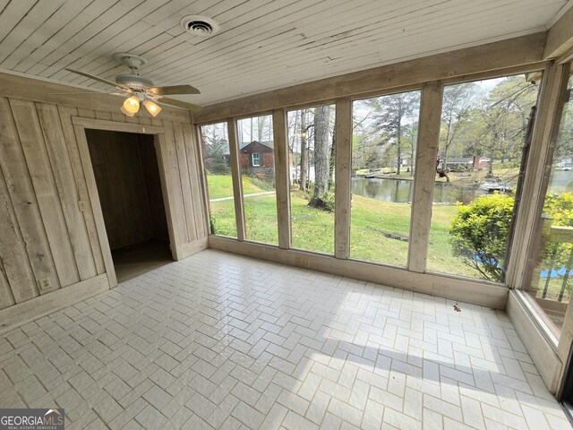unfurnished sunroom with wood ceiling, a ceiling fan, wood walls, visible vents, and a water view
