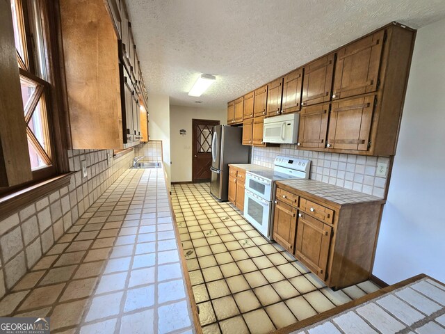 kitchen featuring tasteful backsplash, white appliances, a textured ceiling, a sink, and tile countertops