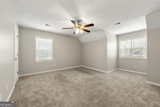 carpeted spare room with a textured ceiling, lofted ceiling, ceiling fan, and visible vents