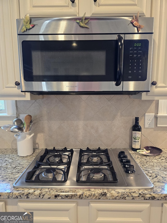 kitchen featuring white cabinets, stainless steel appliances, light stone countertops, and decorative backsplash