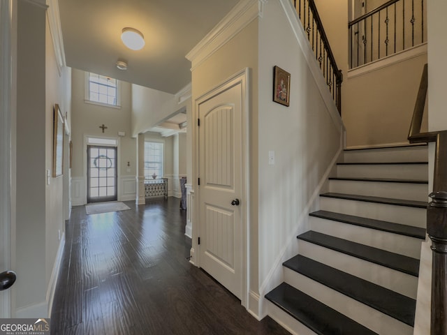 entryway with stairway, a wainscoted wall, a high ceiling, a decorative wall, and dark wood-type flooring