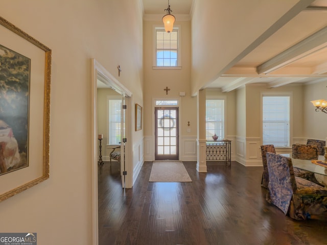 entrance foyer with ornamental molding, dark wood-style flooring, beamed ceiling, a wainscoted wall, and a notable chandelier