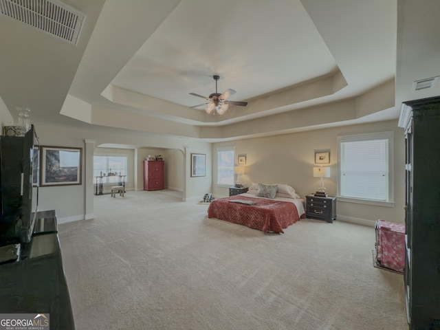 carpeted bedroom with arched walkways, a tray ceiling, visible vents, and baseboards