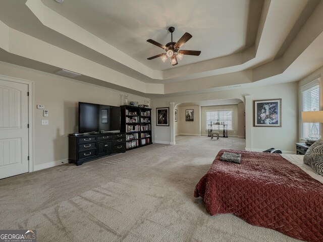 bedroom featuring carpet floors, arched walkways, a tray ceiling, and baseboards