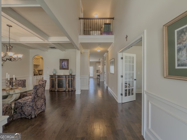 entryway featuring an inviting chandelier, wainscoting, beam ceiling, arched walkways, and dark wood finished floors