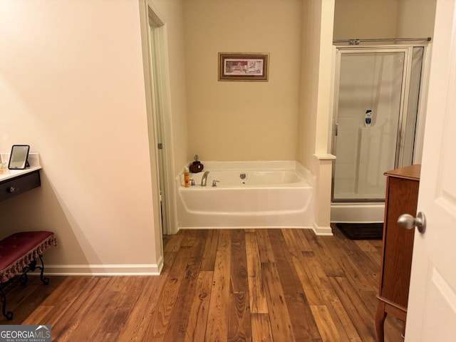 bathroom featuring a stall shower, baseboards, wood finished floors, and a bath