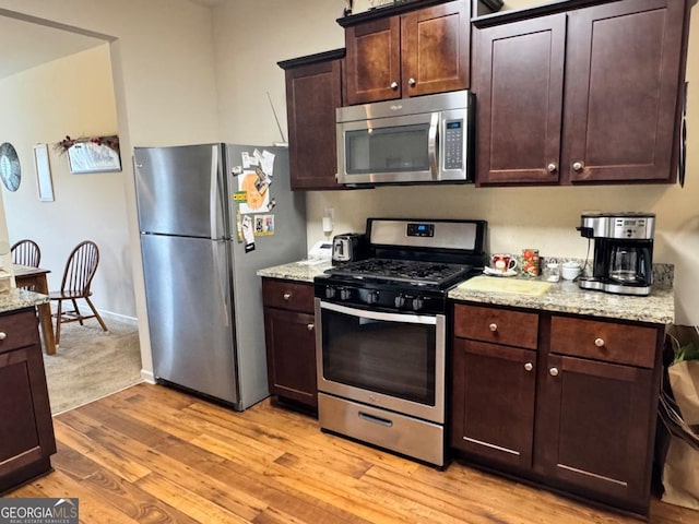kitchen featuring light stone counters, light wood-style flooring, stainless steel appliances, baseboards, and dark brown cabinets
