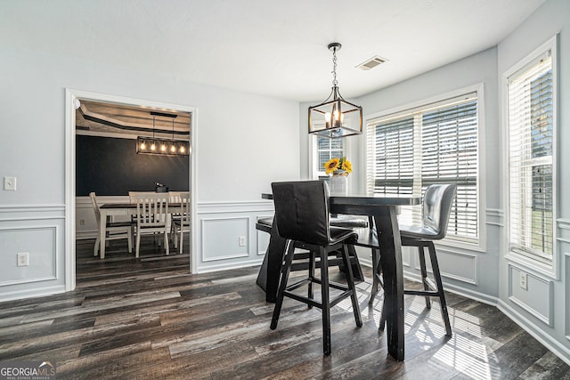 dining space with dark wood-type flooring, a decorative wall, a notable chandelier, and visible vents