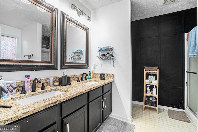 full bath featuring a sink, baseboards, double vanity, and a textured ceiling