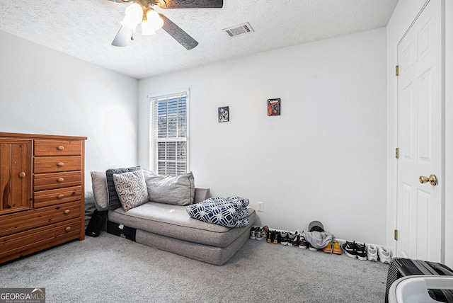 living area with visible vents, ceiling fan, carpet, and a textured ceiling