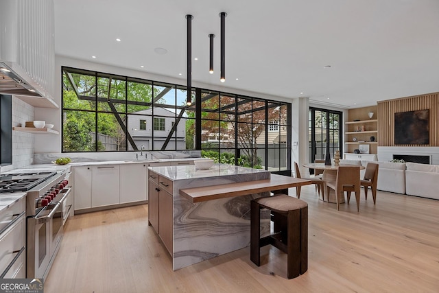 kitchen featuring white cabinetry, double oven range, wall chimney exhaust hood, and light wood-style floors