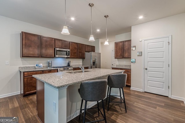 9061 Jim Purcell Dr, Covington, GA 30014 - kitchen featuring appliances with stainless steel finishes, dark wood-style flooring, a breakfast bar area, an island with sink, and light stone countertops