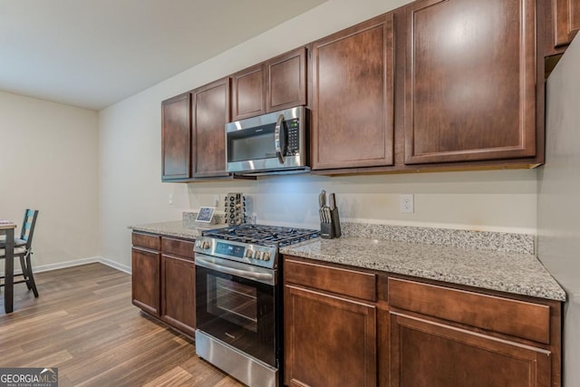 9061 Jim Purcell Dr, Covington, GA 30014 - kitchen featuring stainless steel appliances, light wood-style floors, light stone counters, and dark brown cabinetry