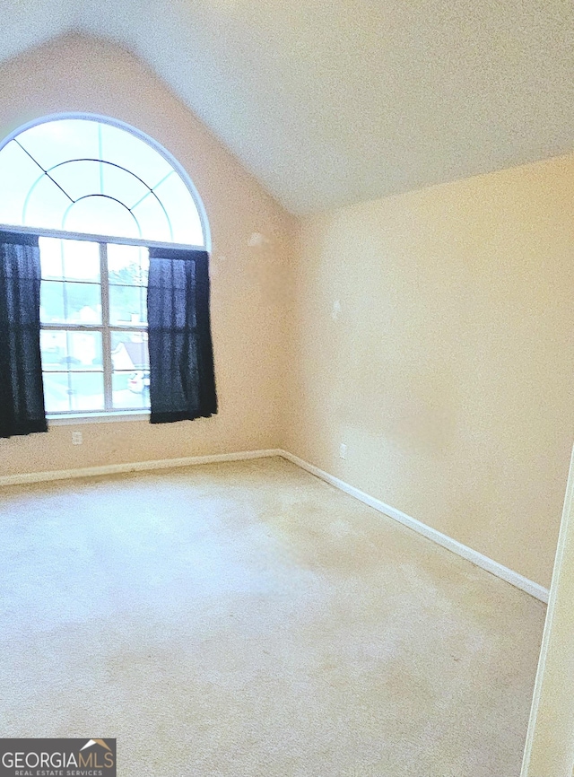 empty room featuring carpet, baseboards, and lofted ceiling