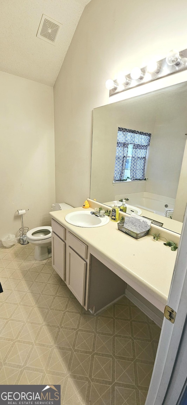 bathroom featuring visible vents, toilet, vanity, tile patterned floors, and lofted ceiling