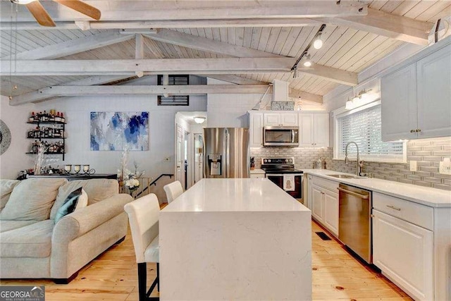 kitchen with light wood finished floors, a breakfast bar, appliances with stainless steel finishes, a sink, and backsplash