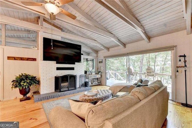 living area featuring a brick fireplace, lofted ceiling with beams, wood finished floors, and a ceiling fan