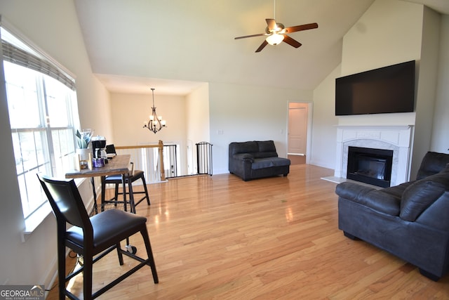 living area with a premium fireplace, high vaulted ceiling, light wood-type flooring, baseboards, and ceiling fan with notable chandelier