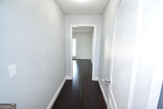 hallway featuring a textured ceiling, baseboards, and dark wood finished floors