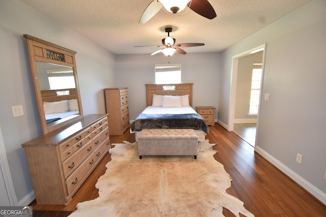 bedroom with a textured ceiling, a ceiling fan, wood finished floors, and baseboards