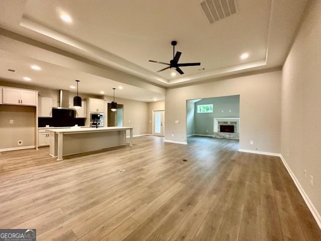 149 Sagebrook Ln Lot 8, Newnan, GA 30263 - unfurnished living room with a tray ceiling, light wood finished floors, a fireplace with raised hearth, ceiling fan, and recessed lighting