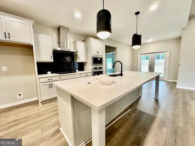 149 Sagebrook Ln Lot 8, Newnan, GA 30263 - kitchen featuring wall chimney range hood, french doors, an island with sink, light wood-style floors, and recessed lighting