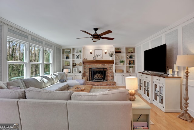 1135 Parkview Way, Lilburn, GA 30047 - living area featuring light wood-style floors, built in shelves, ceiling fan, a brick fireplace, and crown molding