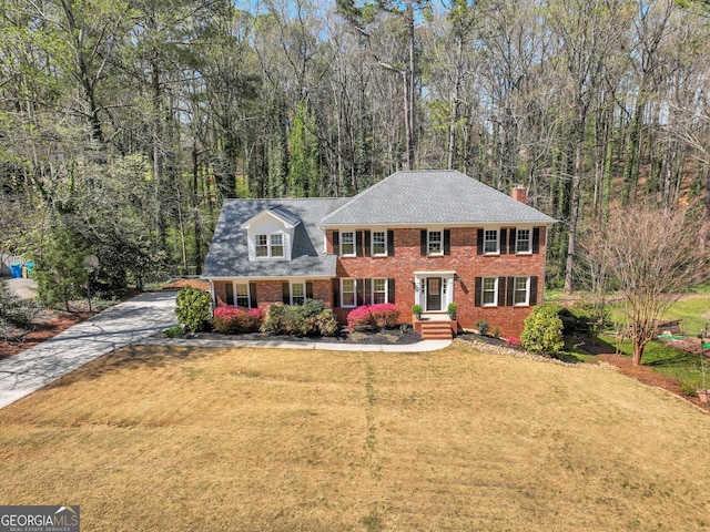1135 Parkview Way, Lilburn, GA 30047 - colonial house with a front lawn, a chimney, a forest view, brick siding, and concrete driveway