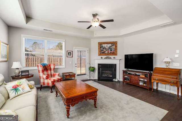 2910 Bishopstone Way, Cumming, GA 30040 - living area with dark wood-style flooring, a ceiling fan, a fireplace with flush hearth, visible vents, and a raised ceiling