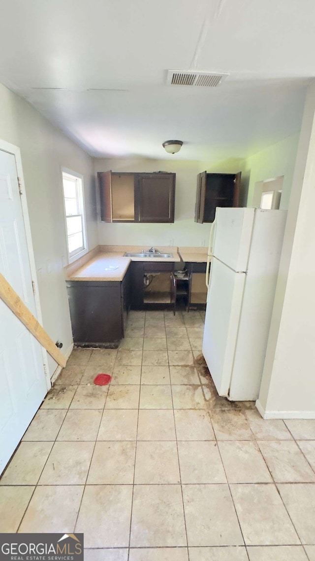 kitchen featuring light tile patterned flooring, light countertops, freestanding refrigerator, baseboards, and visible vents