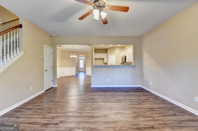 unfurnished living room featuring dark wood-style flooring, ceiling fan with notable chandelier, baseboards, and stairs